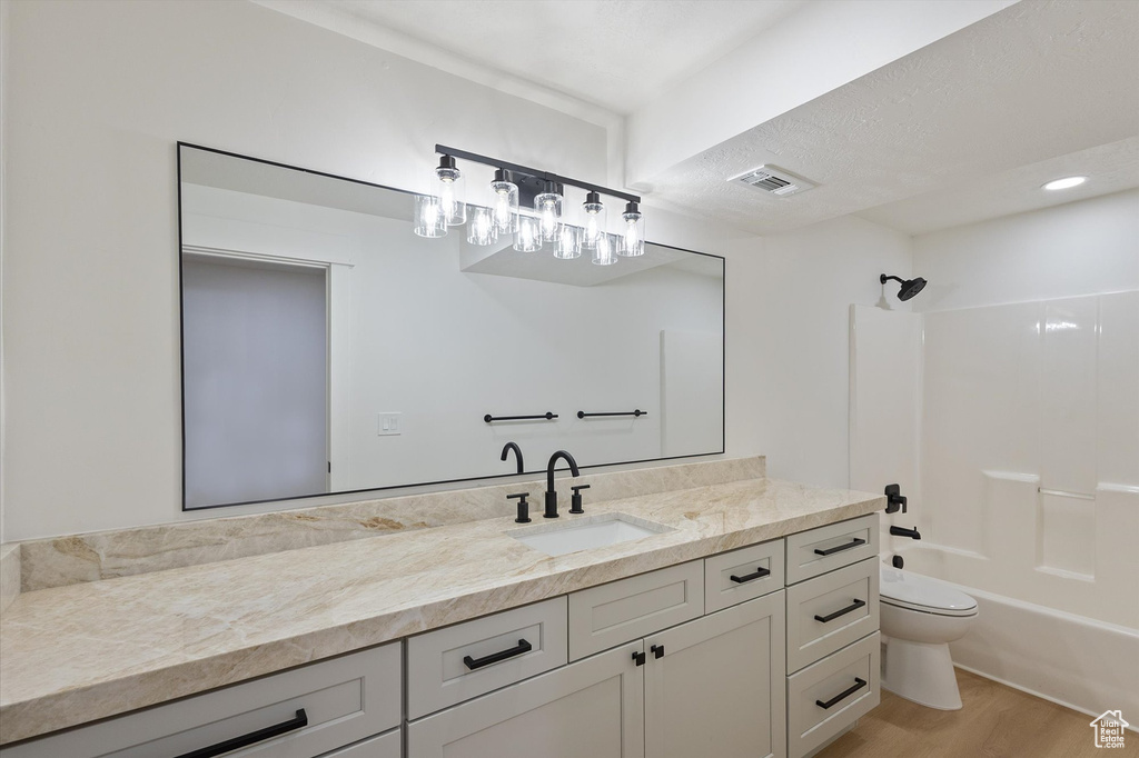 Bathroom featuring wood finished floors, toilet, vanity, and washtub / shower combination