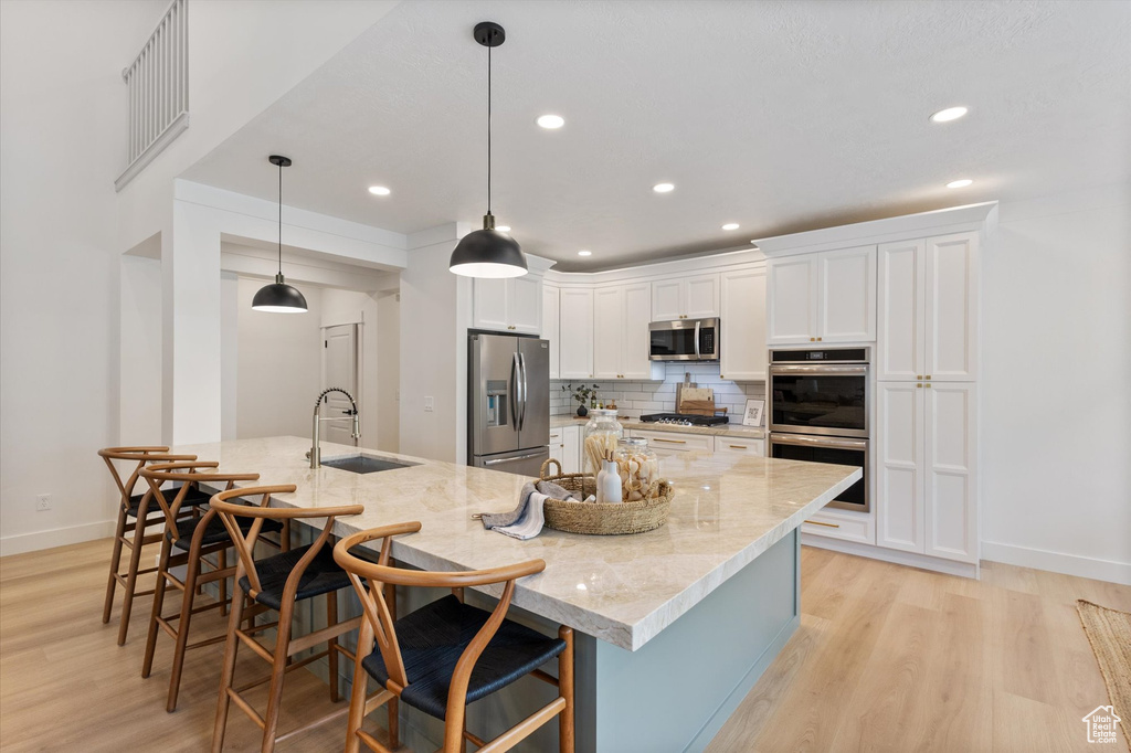 Kitchen featuring stainless steel appliances, a sink, light wood finished floors, white cabinets, and tasteful backsplash
