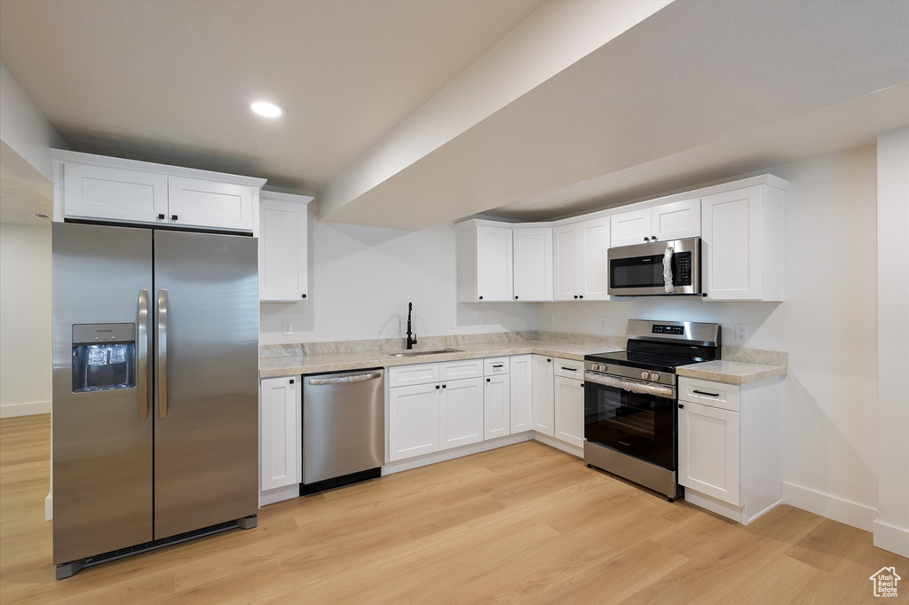 Kitchen with appliances with stainless steel finishes, a sink, light wood-style floors, light countertops, and white cabinets