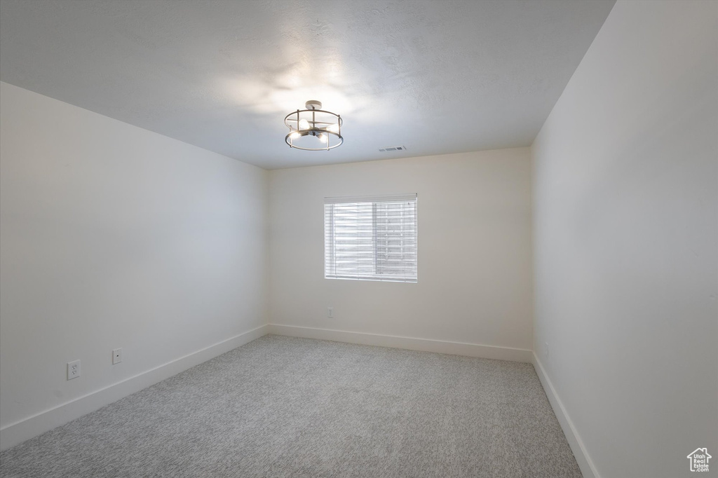 Spare room featuring light carpet, baseboards, and a chandelier