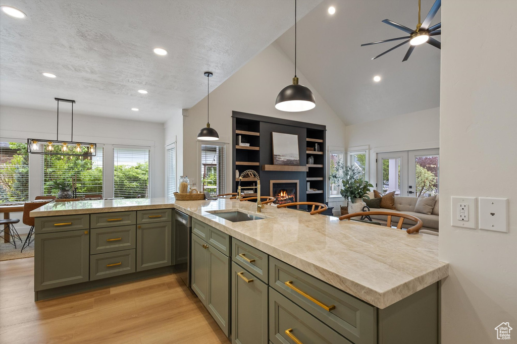 Kitchen featuring open floor plan, stainless steel dishwasher, recessed lighting, a lit fireplace, and light wood-style flooring
