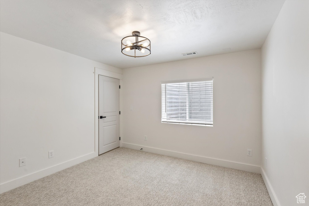 Spare room with light carpet, a chandelier, and baseboards