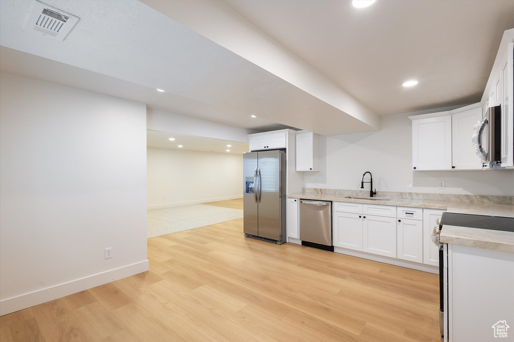 Kitchen featuring stainless steel appliances, a sink, light wood-type flooring, light countertops, and baseboards