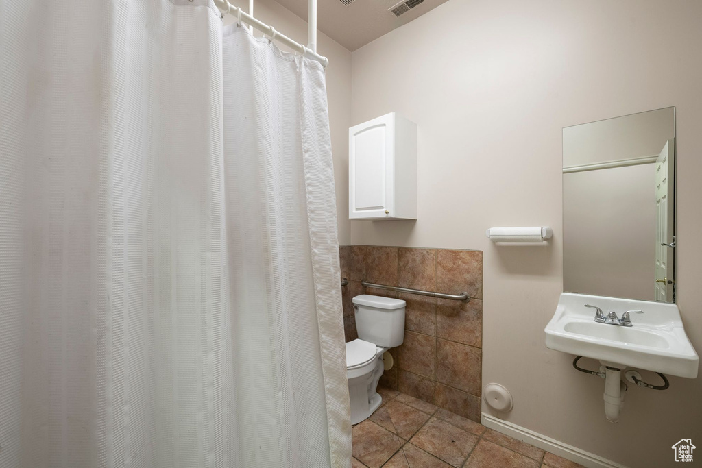 Bathroom with toilet, tile walls, tile patterned flooring, and a sink