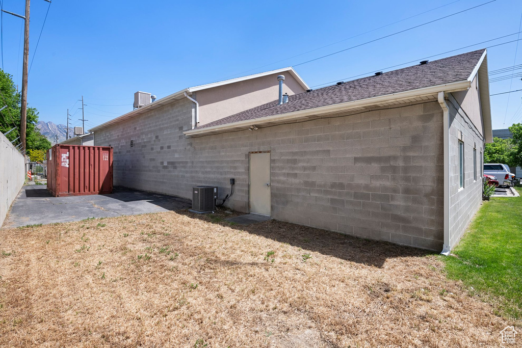 Back of property with concrete block siding, central AC, and roof with shingles