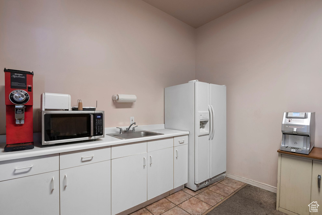 Kitchen featuring stainless steel microwave, a sink, white fridge with ice dispenser, light countertops, and white cabinets