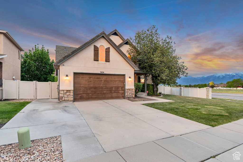 French country inspired facade with stone siding, stucco siding, a garage, driveway, and a mountain view