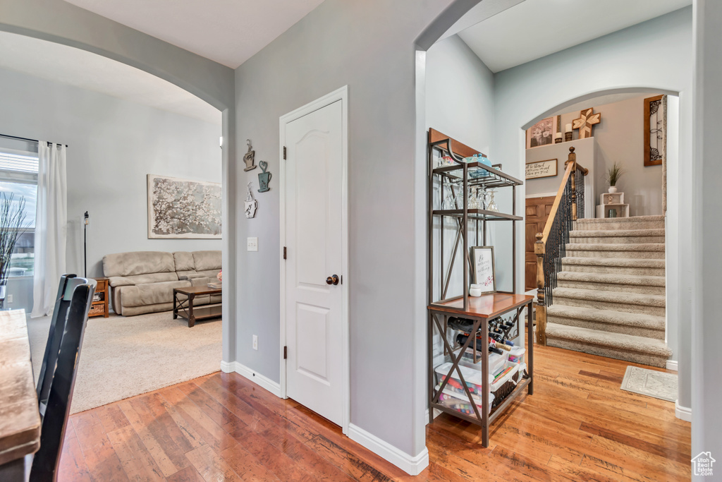 Hall with arched walkways, wood-type flooring, stairs, and baseboards