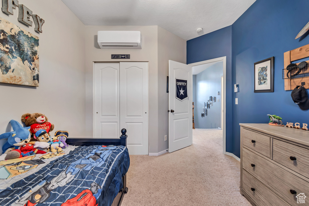 Bedroom with a wall unit AC, light colored carpet, a closet, and baseboards