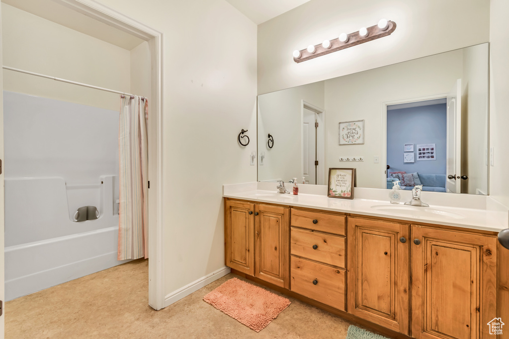 Ensuite bathroom featuring double vanity, shower / tub combo with curtain, and baseboards