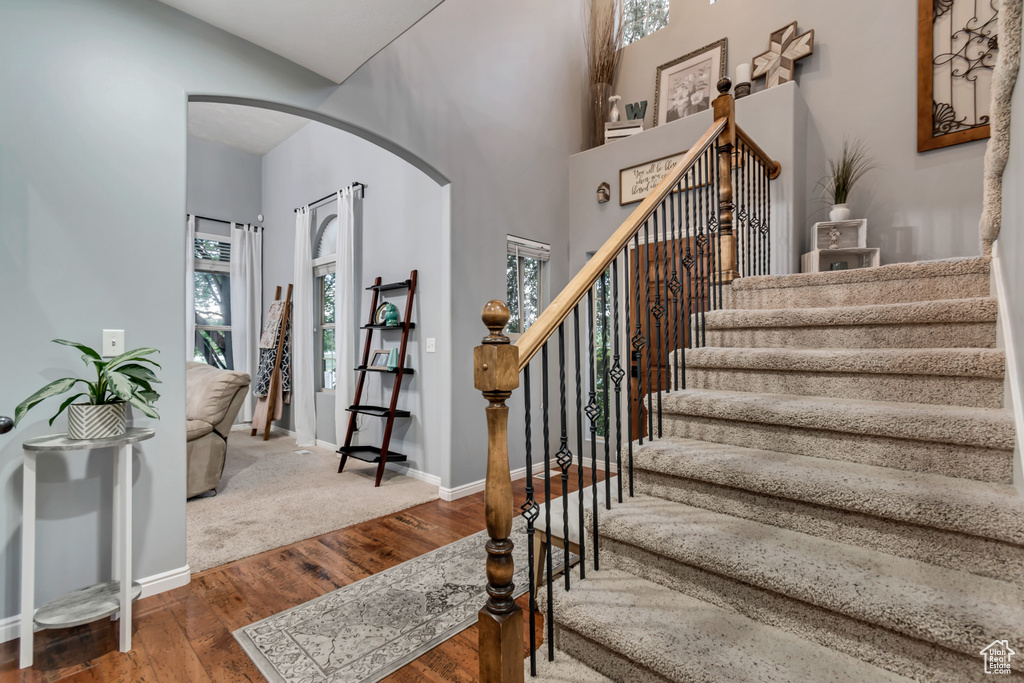 Staircase featuring arched walkways, wood finished floors, baseboards, and a high ceiling