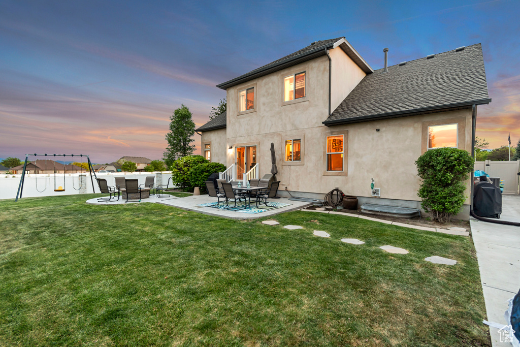 Back of house at dusk featuring stucco siding, a patio area, and roof with shingles