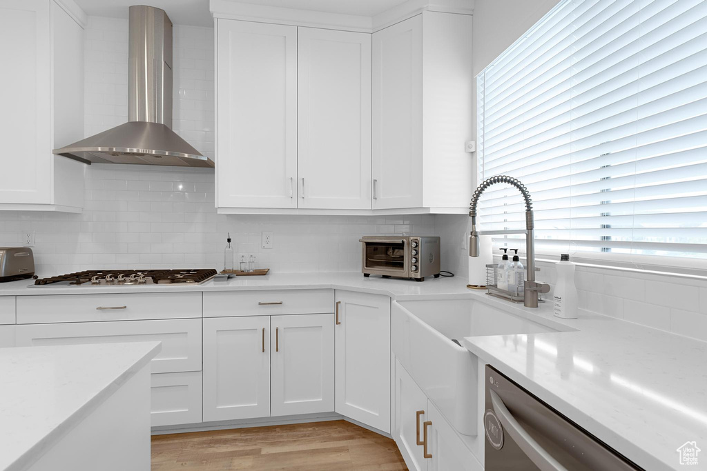 Kitchen with wall chimney exhaust hood, stainless steel dishwasher, gas cooktop, and decorative backsplash