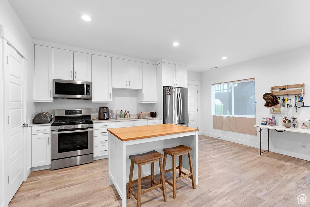 Kitchen featuring stainless steel appliances, butcher block countertops, a kitchen breakfast bar, light wood-type flooring, and recessed lighting