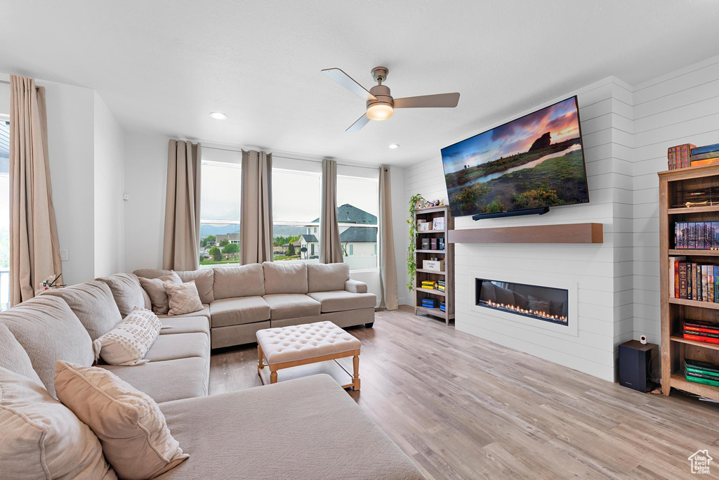 Living area with wood finished floors, a ceiling fan, a glass covered fireplace, recessed lighting, and wood walls