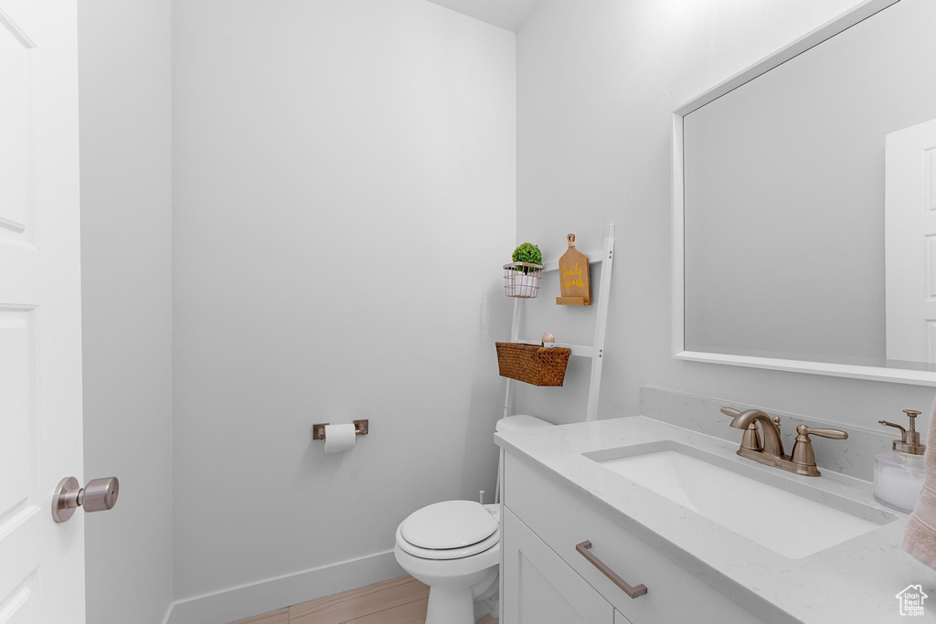 Half bath featuring toilet, vanity, wood finished floors, and baseboards