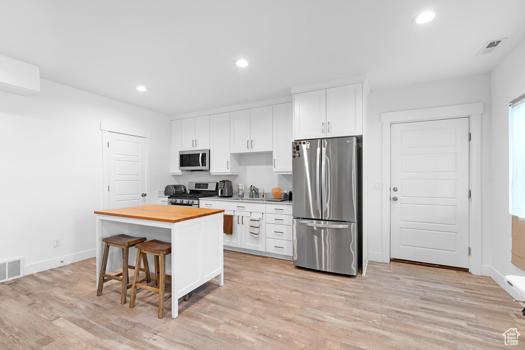 Kitchen featuring appliances with stainless steel finishes, butcher block counters, white cabinets, and recessed lighting