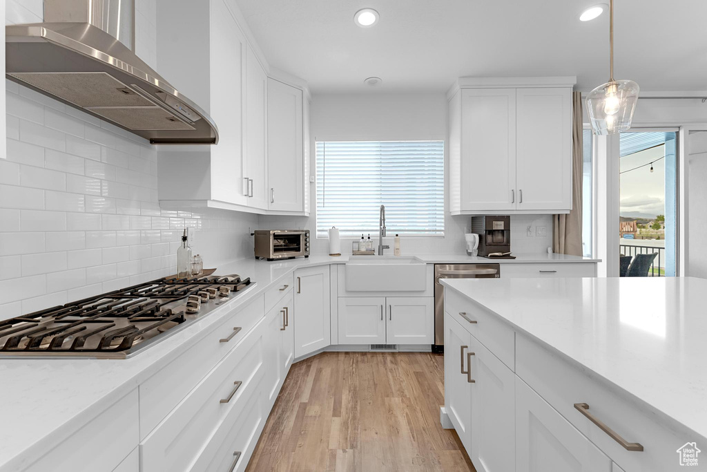 Kitchen featuring appliances with stainless steel finishes, wall chimney exhaust hood, a sink, light countertops, and white cabinets
