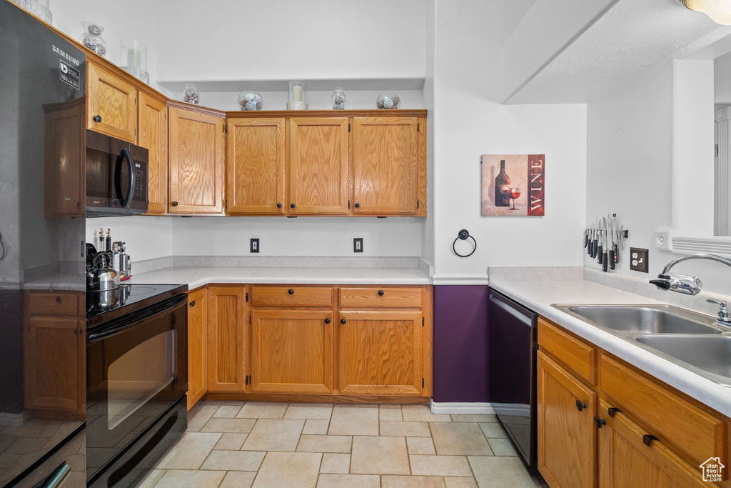 Kitchen featuring black appliances, a sink, light countertops, and brown cabinets