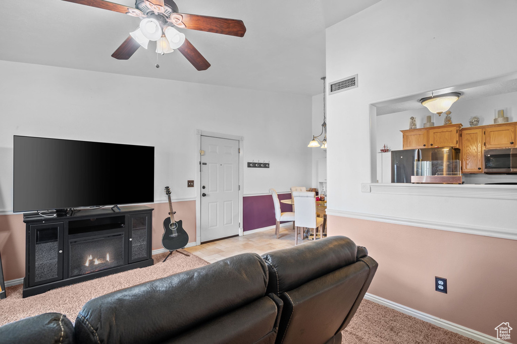 Living room with baseboards, a ceiling fan, light carpet, and a glass covered fireplace
