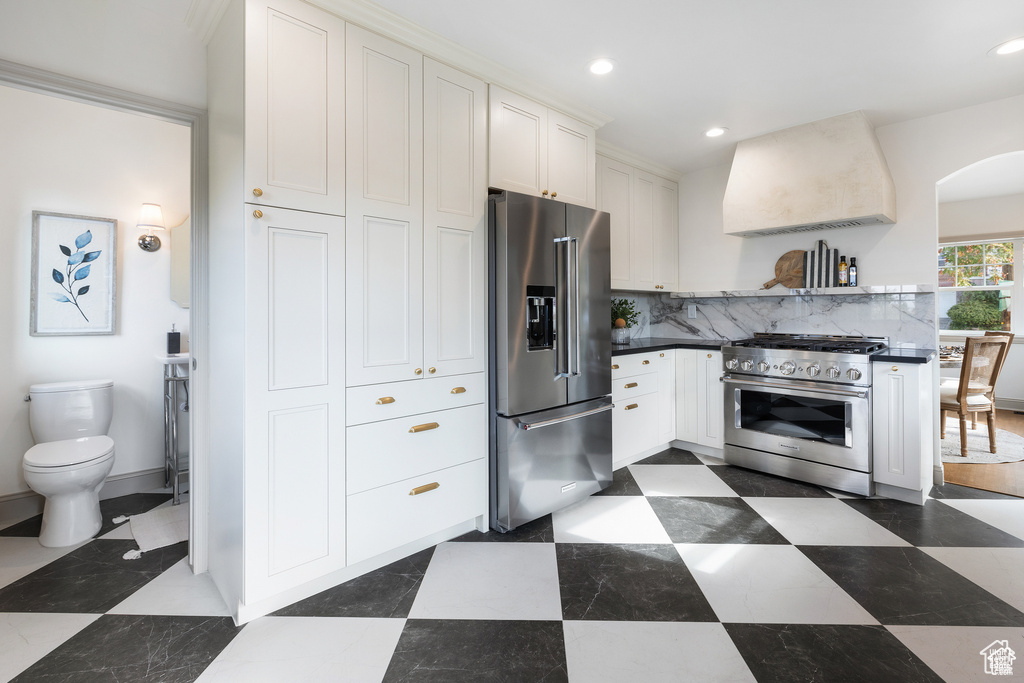 Kitchen featuring high quality appliances, wall chimney range hood, recessed lighting, tasteful backsplash, and white cabinetry