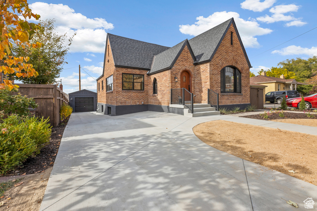 Tudor-style house featuring brick siding, concrete driveway, a shingled roof, an outbuilding, and a detached garage