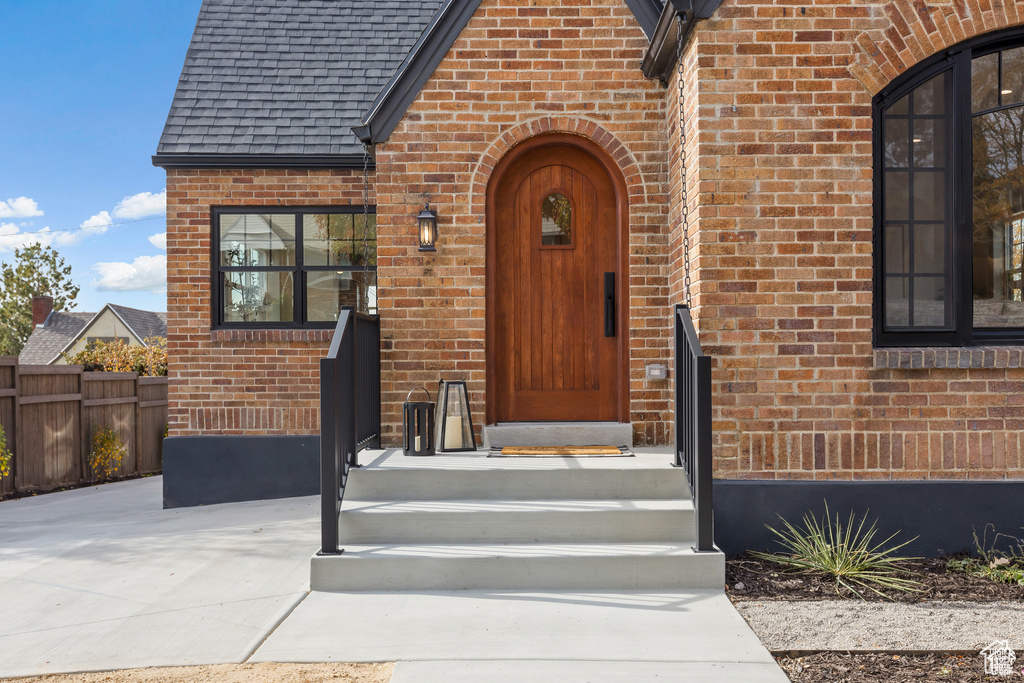Property entrance featuring brick siding, fence, and a shingled roof
