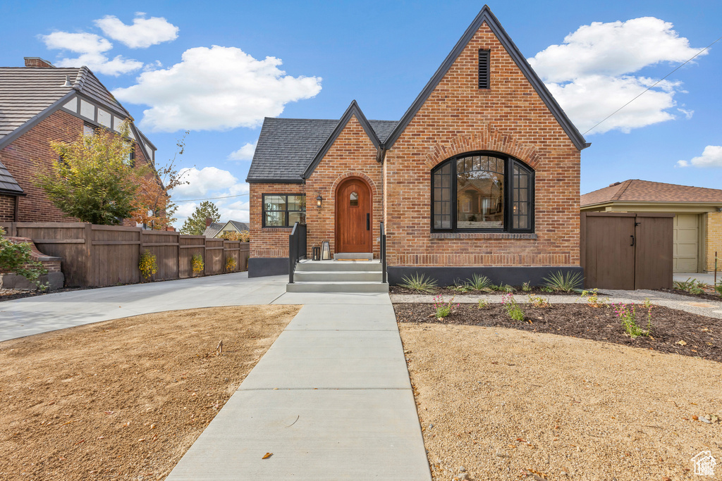 Tudor-style house featuring brick siding, fence, and a shingled roof