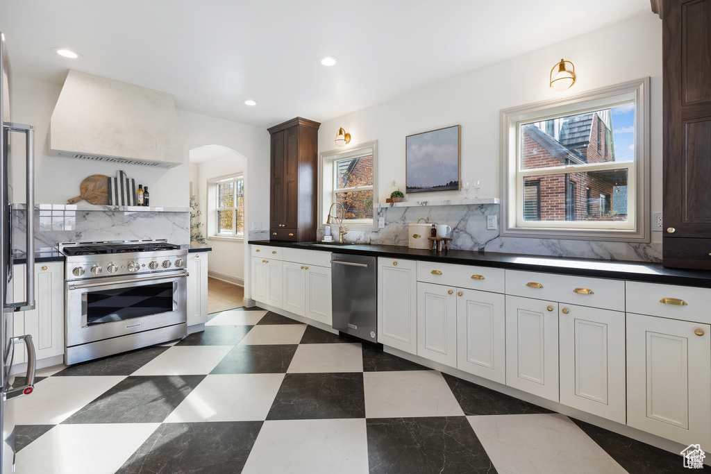Kitchen with appliances with stainless steel finishes, extractor fan, arched walkways, a sink, and backsplash