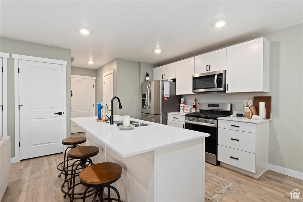 Kitchen with stainless steel appliances, a sink, light wood-style floors, a kitchen island with sink, and a breakfast bar area