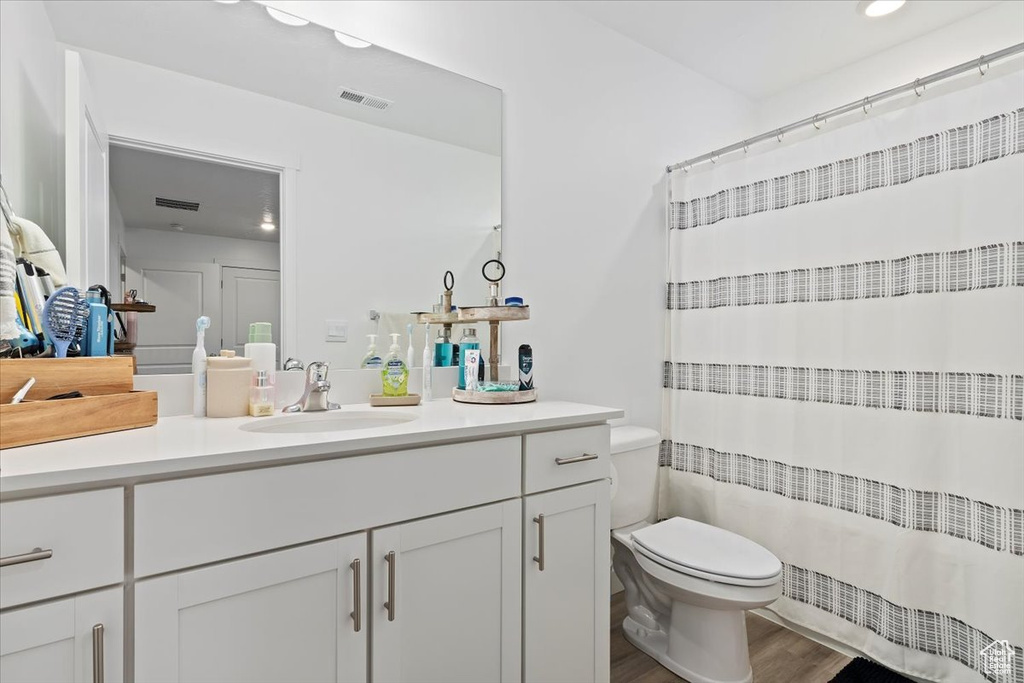 Bathroom with toilet, wood finished floors, vanity, a shower with curtain, and recessed lighting