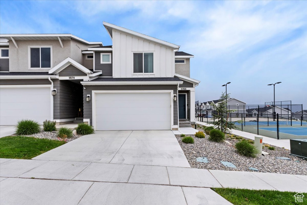 View of front facade featuring fence, a tennis court, a garage, driveway, and board and batten siding
