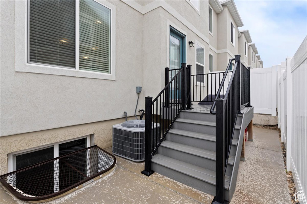 View of exterior entry with fence, stucco siding, and cooling unit