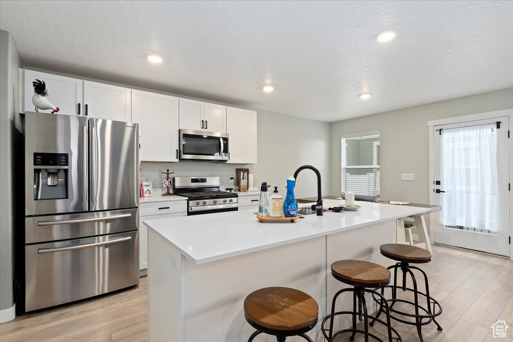 Kitchen featuring stainless steel appliances, light wood-type flooring, a kitchen bar, white cabinetry, and recessed lighting