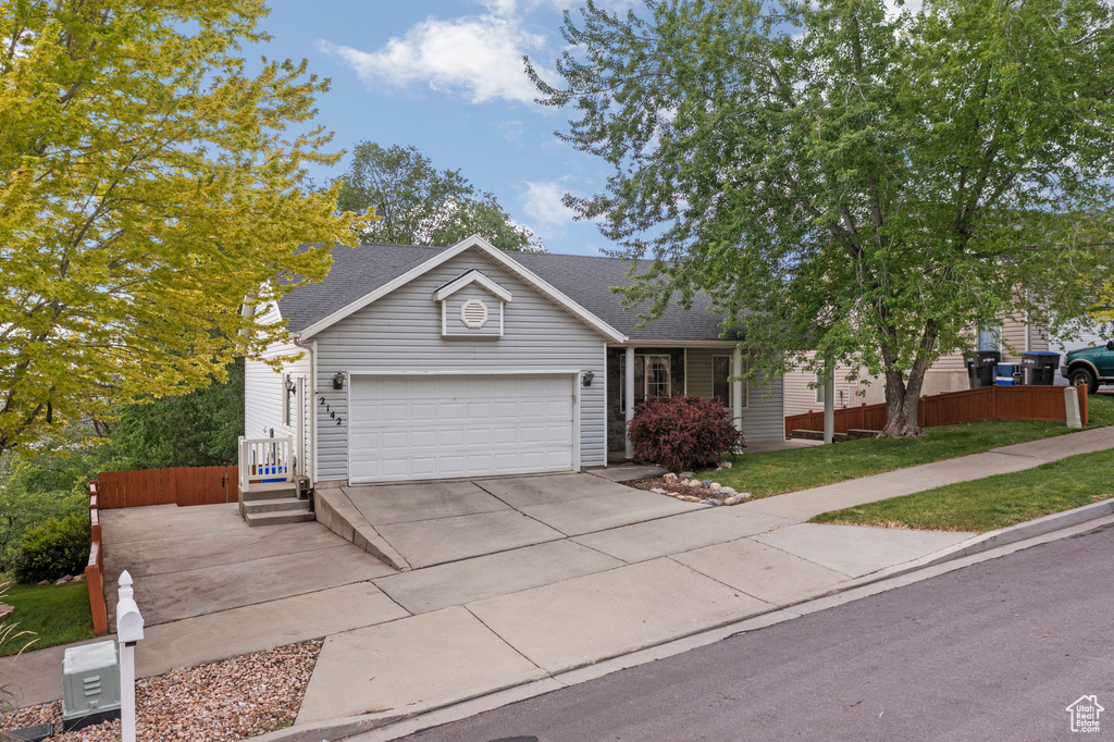 View of front of property with concrete driveway, a garage, a shingled roof, and a front lawn