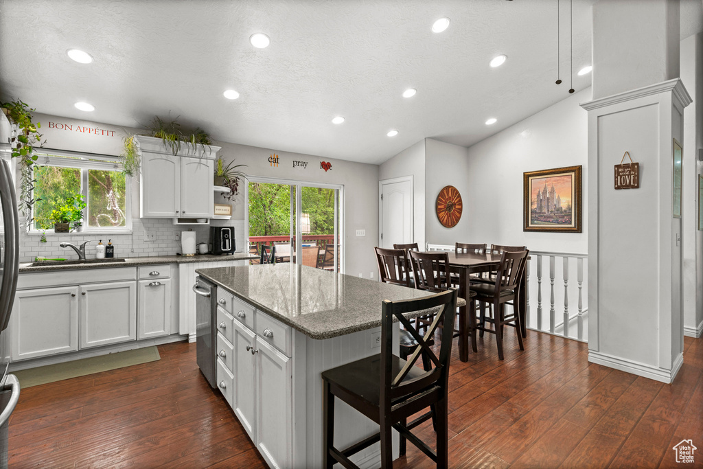 Kitchen featuring dark wood-type flooring, a kitchen island, white cabinets, a sink, and dark stone countertops