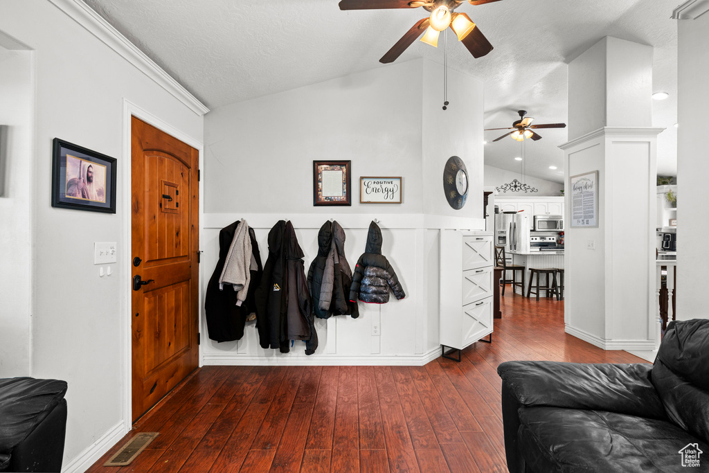 Entrance foyer with vaulted ceiling, a ceiling fan, dark wood-style flooring, and wainscoting
