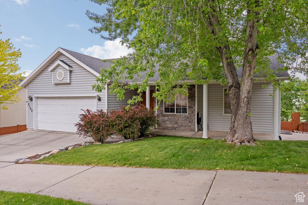 View of front of home with concrete driveway, a shingled roof, covered porch, a front lawn, and an attached garage