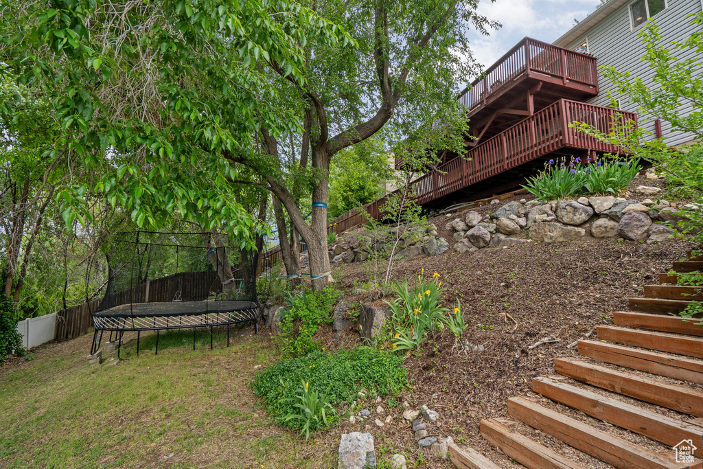 View of yard featuring stairs, a trampoline, and a wooden deck