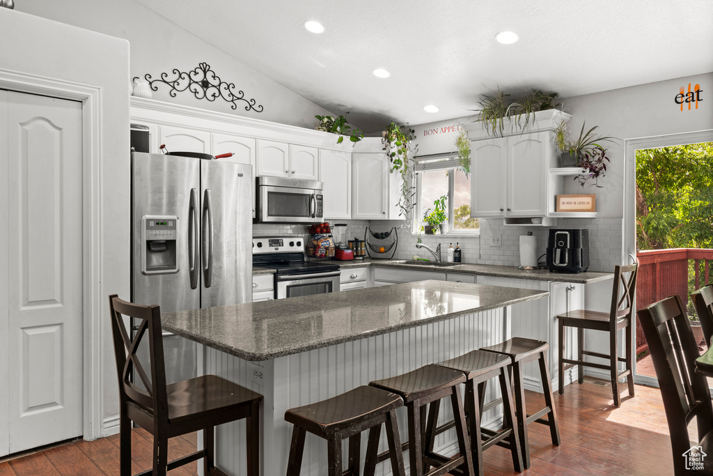Kitchen with stainless steel appliances, a sink, backsplash, white cabinetry, and a kitchen bar