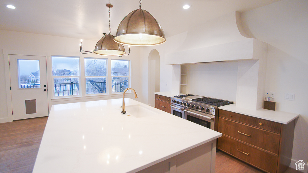 Kitchen with a sink, double oven range, wood finished floors, light countertops, and arched walkways