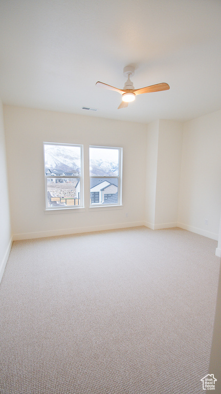 Empty room with light colored carpet, baseboards, and a ceiling fan