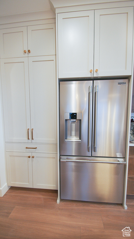 Detailed view of high quality fridge, light wood-type flooring, white cabinetry, and baseboards