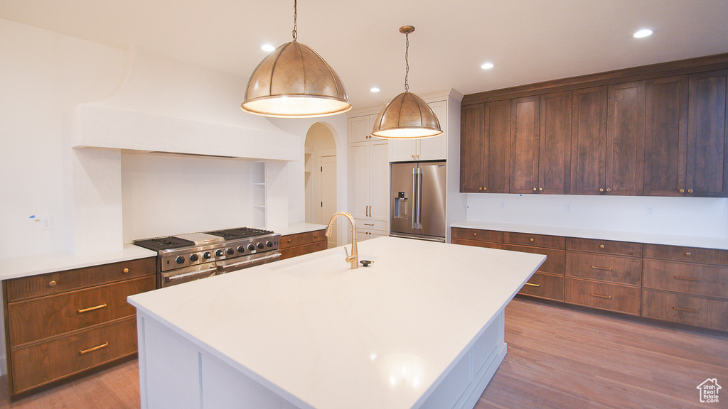 Kitchen featuring high end refrigerator, a sink, range, light wood-style floors, and light countertops