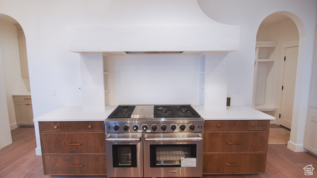 Kitchen featuring double oven range, wood finished floors, arched walkways, and light countertops
