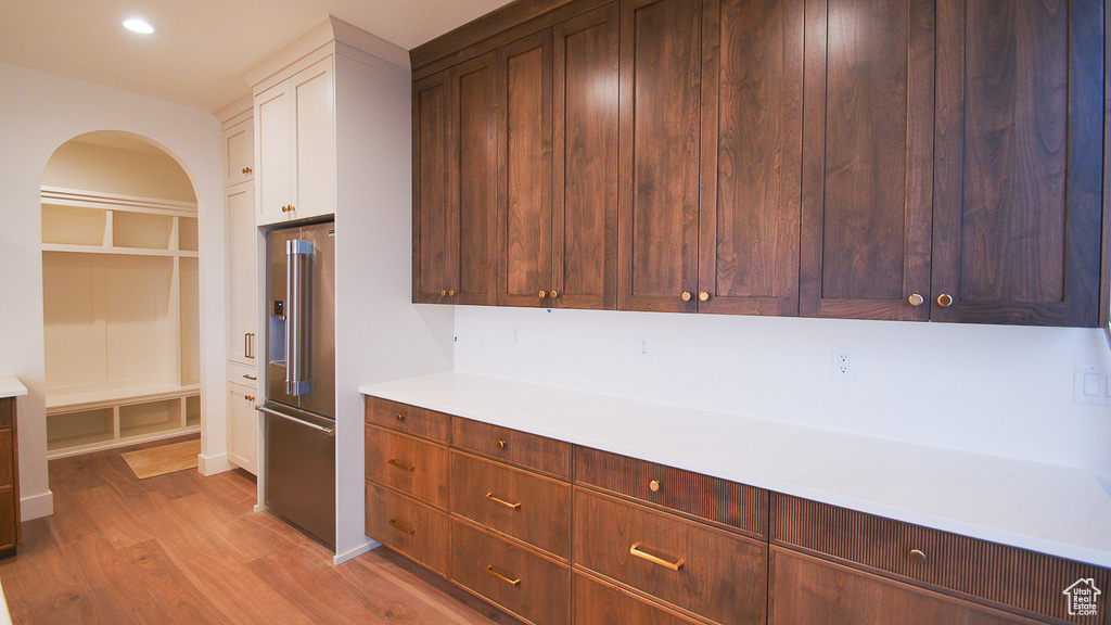 Kitchen with high end fridge, light wood-style floors, arched walkways, light countertops, and white cabinets