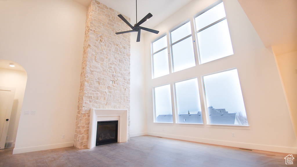 Unfurnished living room with a towering ceiling, a ceiling fan, a large fireplace, plenty of natural light, and wood finished floors