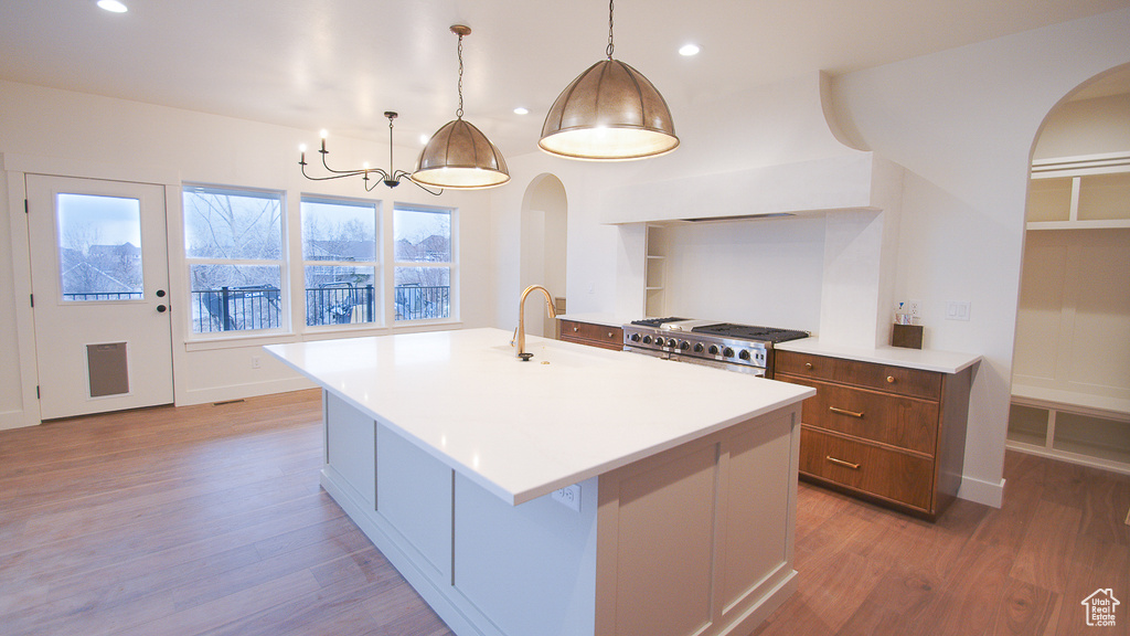 Kitchen with stove, arched walkways, light wood-style flooring, a sink, and a chandelier