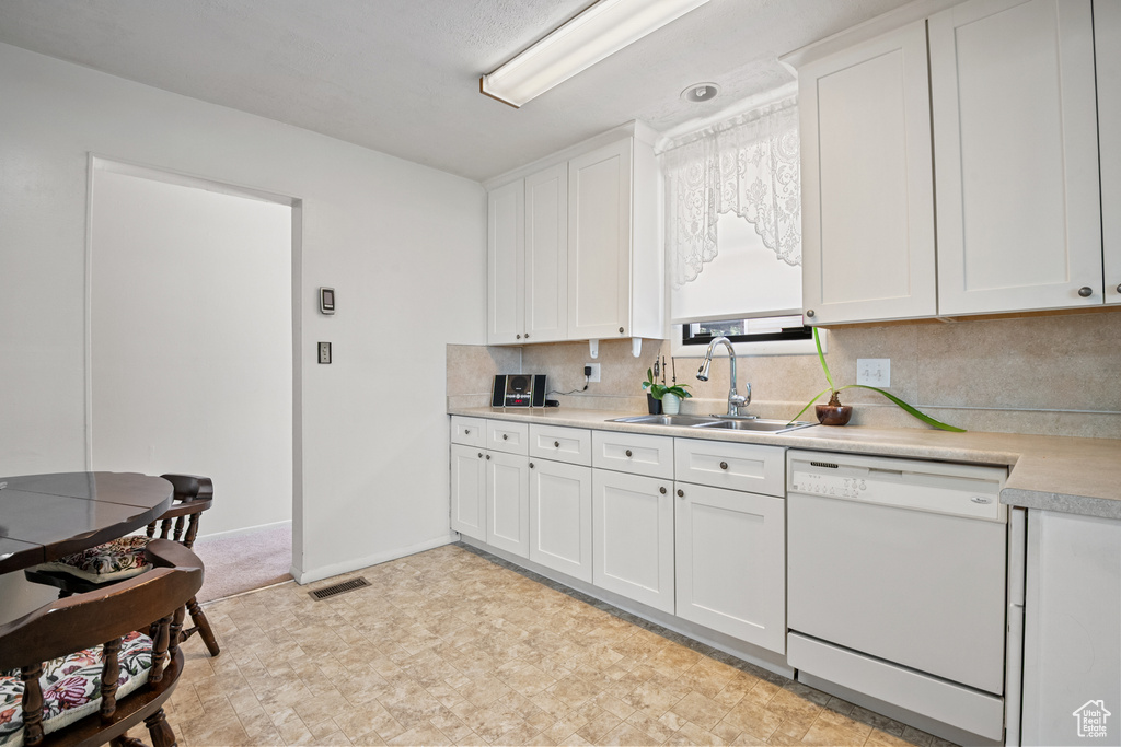 Kitchen featuring white dishwasher, a sink, light countertops, and white cabinetry