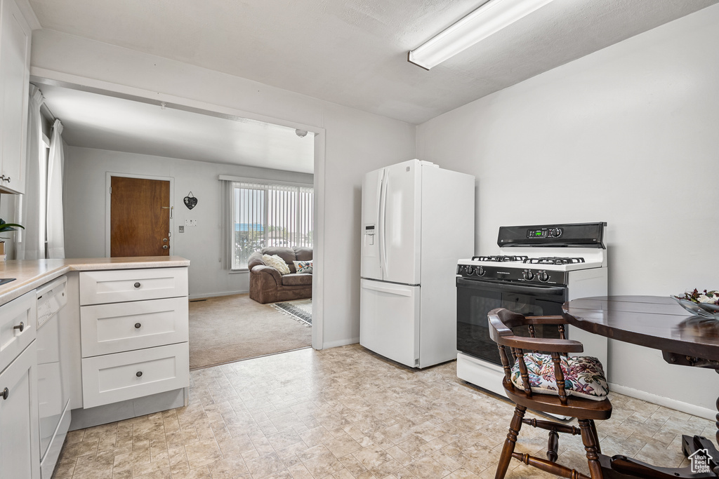 Kitchen featuring white appliances, white cabinetry, baseboards, and light countertops